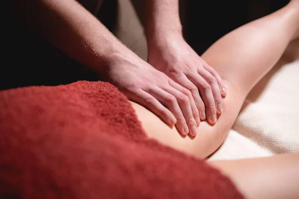 Close-up low key on womans thigh massage in a professional premium spa salon, man masseur does in a dark room — Stock Photo, Image