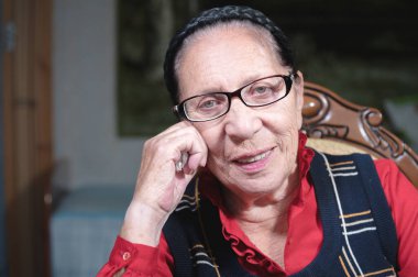 Gözlüklü, gülümseyen yaşlı bir kadın karanlık bir odada koltukta oturur ve üzgün bir şekilde kameraya bakar. Bir salgın sırasında yaşlı insanların virüsten korunması ve kurtarılması kavramı