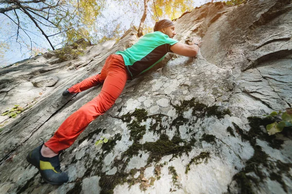 Мужчина в возрасте 40 лет занимается альпинизмом, тренируется в одиночестве на высокой скале в лесу. Концепция активного отдыха для людей старше 40 лет — стоковое фото