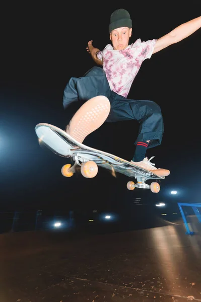 Un giovane skatecrack in uno skatepark notturno fa un salto con l'halfpipe. Cultura giovanile Concetto di svago di notte — Foto Stock