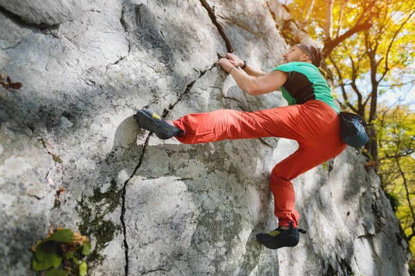 Мужчина в возрасте 40 лет занимается альпинизмом, тренируется в одиночестве на высокой скале в лесу. Концепция активного отдыха для людей старше 40 лет — стоковое фото