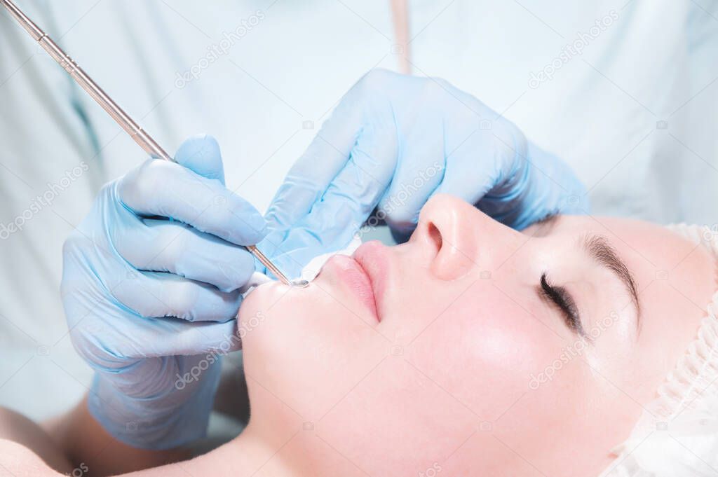 Close-up Mechanical face peel at the beautician. Beautician squeezes acne on the patients forehead with a medical needle. Face next to hands in blue gloves of cosmologist