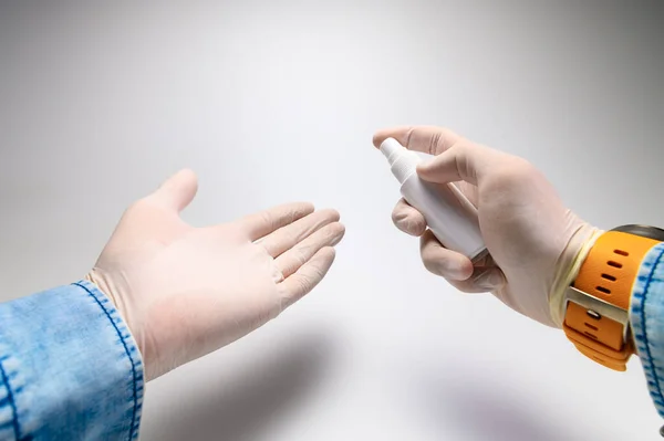 Close-up self-treatment of hands with an antiseptic with an aerosol first-person view. Mens hands in white medical gloves, a blue denim shirt — Stock Photo, Image