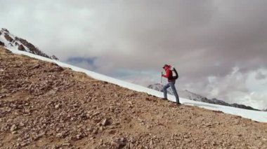 Güneş gözlüklü, uzun saçlı, havadar görünümlü genç bir adam. Rbczak 'ı olan bir adam, dağların tepesinde, kar vardiyasının yanındaki kayalıklara tırmanıyor..