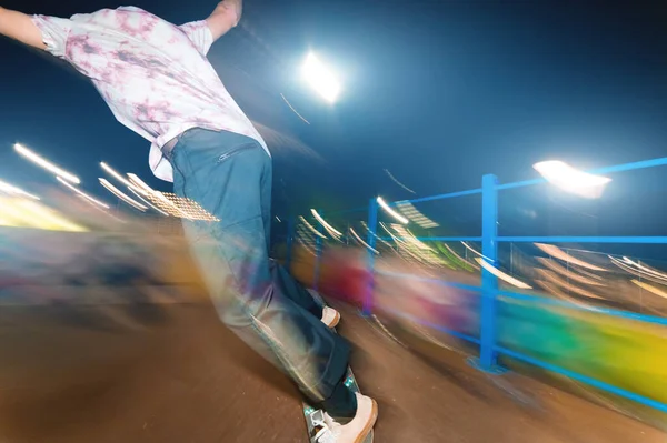 Jeune patineur élégant dans un chapeau à la mode chevauche un skatepark la nuit. Photo de nuit avec le mouvement des lumières et flou . — Photo