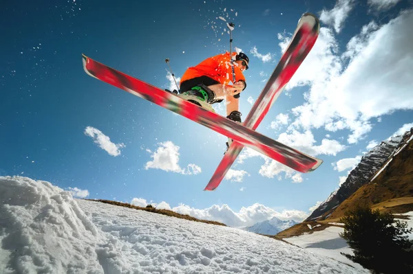 Un jeune athlète skieur fait un tour sur un saut de kicker de neige et des skis de cross dans un contre-jour contre un ciel bleu et des nuages dans les montagnes . — Photo