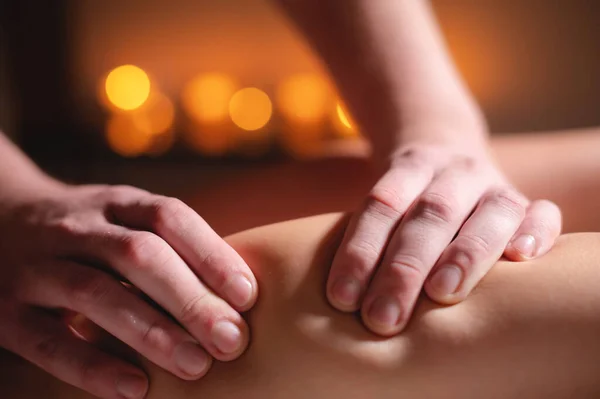 Närbild professionell kalv muskel massage till en kvinnlig klient av en manlig sjukgymnast i en massage salong i ett mörkt kontor mot bakgrund av brinnande ljus — Stockfoto