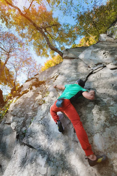 A man is training in free climbing on a rock stone in the forest on a sunny day. The concept of leisure activities of an active lifestyle of people aged — Stock Photo, Image