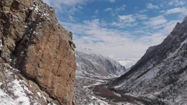 Una vista aérea de la envergadura junto a la roca en el desfiladero de la montaña a principios de primavera empolvada de nieve. — Vídeo de stock