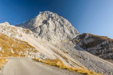 Sonbaharda Mangart 'a giden eski asfalt yol. Yıpranmış beton yığınları ve arka planda Mangart zirvesi. Slovenya.