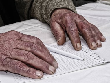 Kalem ve kağıt tutan adamın yeşil kazak giydiğini kırışmış eller closeup