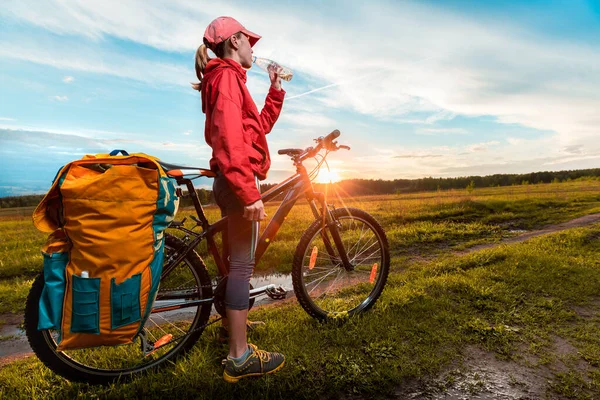 年轻的骑自行车的女徒步旅行者站在草地上潮湿的乡间路上 — 图库照片