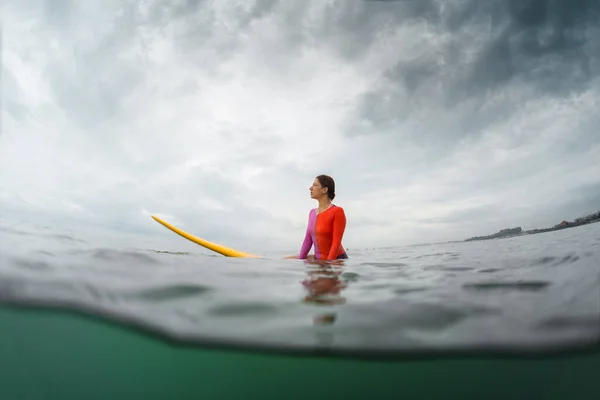 波を待っているボード上に座っている若い女性サーファーの水中分割ショット — ストック写真