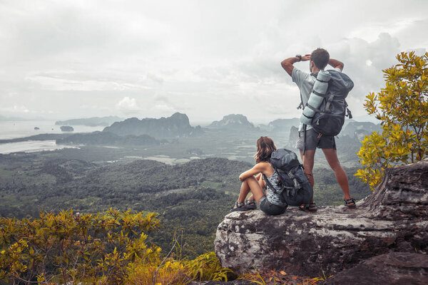 Пара туристов с рюкзаками, отдыхающих на вершине горы и наслаждающихся видом на долину
