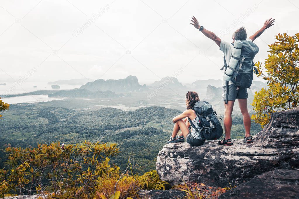 Couple with backpacks relaxing on top of a mountain and enjoying the view of valley