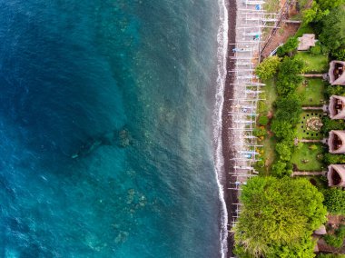 Japon gemi enkazının hava görüntüsü sahile yakın battı. Sahilde geleneksel kayıklar ve yeşil bahçeli bungalovlar, Bali adası, Endonezya