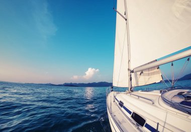 Yelkenli gemi yelkenlerin altından adaya doğru ilerliyor.