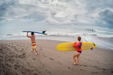 Sahilde sörf tahtasıyla yürüyen iki sörfçü.