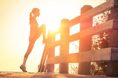 Sıska genç kadın gün doğumunda esneme egzersizleri yapıyor.