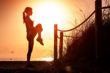 Gün doğumunda kumsalda esneme egzersizleri yapan bir kadın.