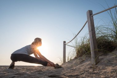 Gün doğumunda kumsalda esneme egzersizleri yapan bir kadın.