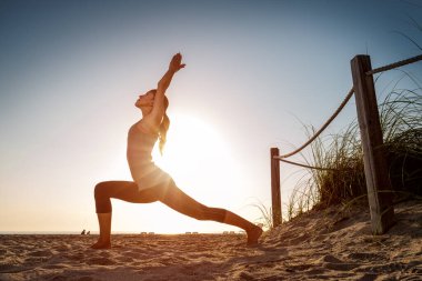 Gün doğumunda kumsalda esneme egzersizleri yapan bir kadın.