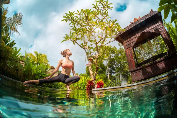 若いです女性は プールによって熱帯の庭でヨガの演習を実行します — ストック写真
