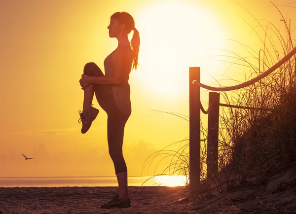 妇女在日出时在海滩上进行伸展运动 — 图库照片