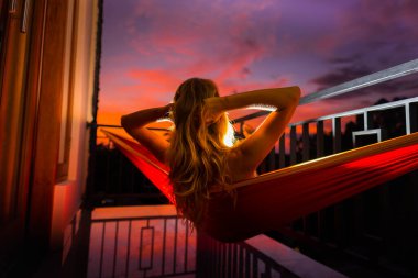 Hamakta dinlenen ve balkondan gün batımının keyfini çıkaran bir kadın.