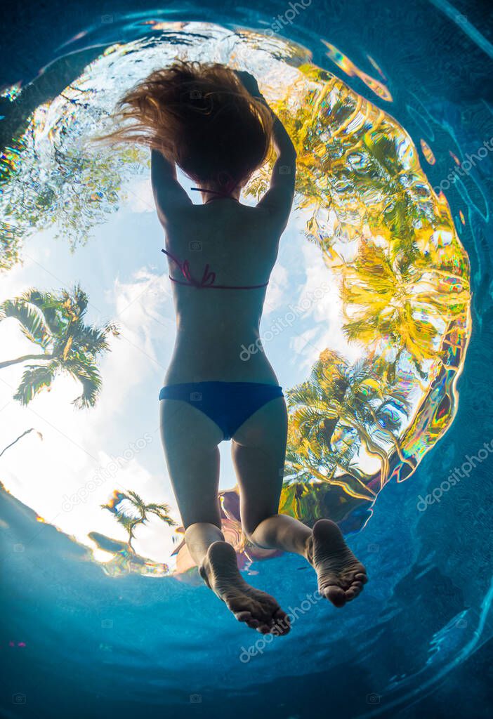 Underwater shot of the woman relaxing in the pool in tropical garden