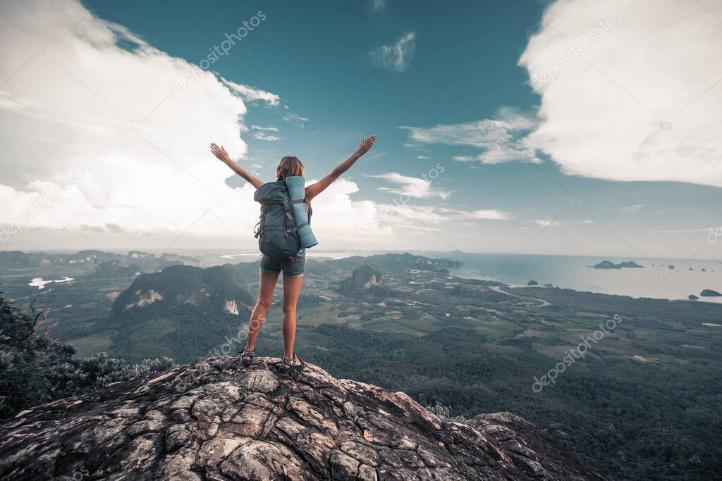 Hiker stands on top of a mountain with raised hands and enjoys valley view