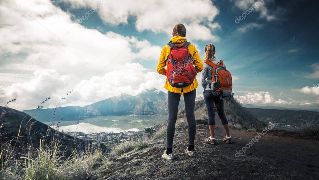 Two hikers stand on the top of a mountain and enjoy valley view
