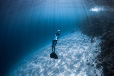 Kadın serbest dalgıç kristal berrak tropikal denizin kumlu tabanında süzülüyor