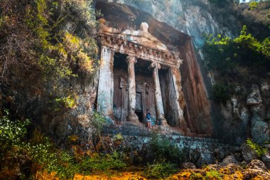 Amyntas kaya mezarları. Dik kayalıklara oyulmuş M.Ö. 4. mezarlar. Turist kapının önünde duruyor. Fethiye, Türkiye.