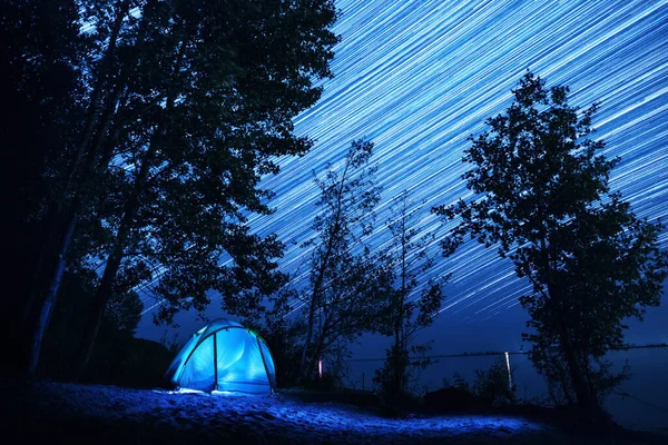 夜空に星の道を持つ川の海岸沿いの木々の間に設置されたテント — ストック写真