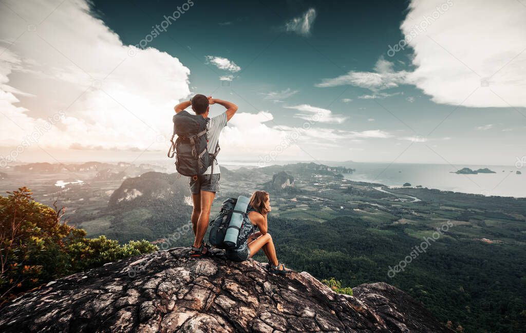 Hikers relax on top of a mountain and enjoy valley greate view