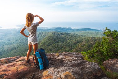 Young woman hiker stands on top of a mountain with raised hands and enjoys sunrise valley view clipart