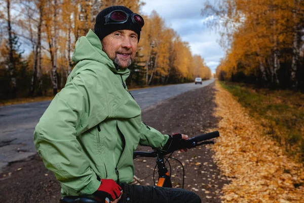 アスファルトの秋の道路上で彼の自転車と成熟した自転車観光客 — ストック写真