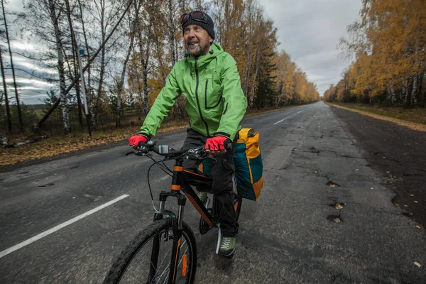 骑着满载自行车的成熟的自行车游客走在一条柏油路上 — 图库照片