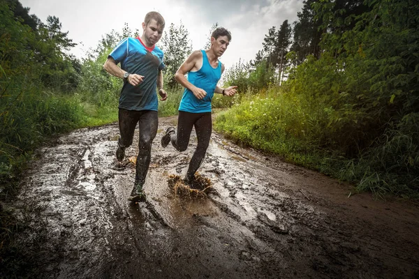 Two athletic sporty men run along the wild muddy rural road