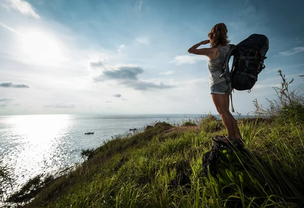 女士徒步旅行者背着背包站在绿色的草地上欣赏海景 — 图库照片