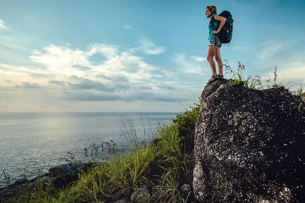 石の上に立って海の景色を楽しむバックパック付きの女性ハイカー — ストック写真