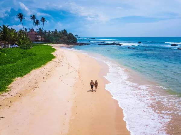 カップルは背景にヤシの木がある熱帯の砂浜を歩く 空中射撃だ 休暇と新婚旅行のコンセプト — ストック写真