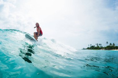 Sörfçü, arka planda palmiye ağaçları ile okyanus dalgalarında sörf yapar.