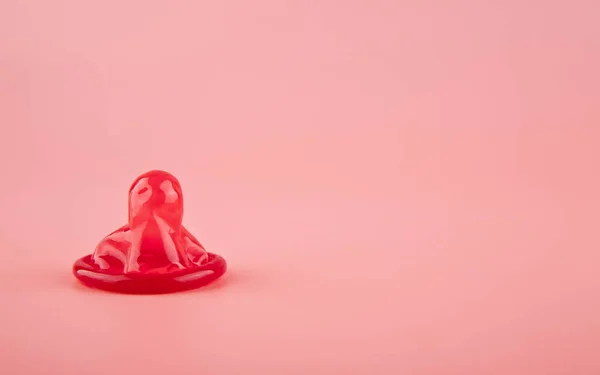 ピンクの背景の赤いコンドームをクローズ アップ — ストック写真