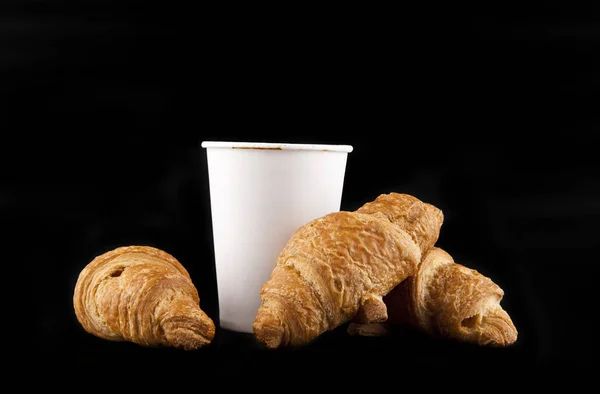 Papper glas med kaffe och croissanter på svart bakgrund — Stockfoto
