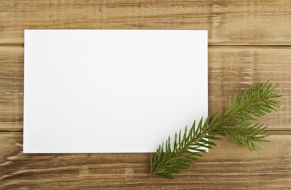 A branch of a Christmas tree and a piece of paper on a wooden ba — Stock Photo, Image