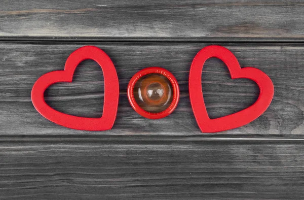 Red hearts and condom on a wooden background — Stock Photo, Image