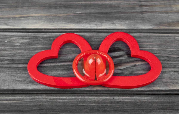 Κόκκινες καρδιές και προφυλακτικό σε φόντο ξύλινη — Φωτογραφία Αρχείου