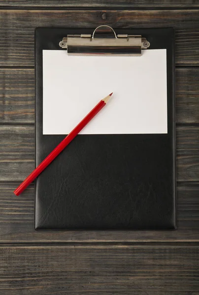 Una tableta para papel y un lápiz rojo sobre un fondo de madera — Foto de Stock